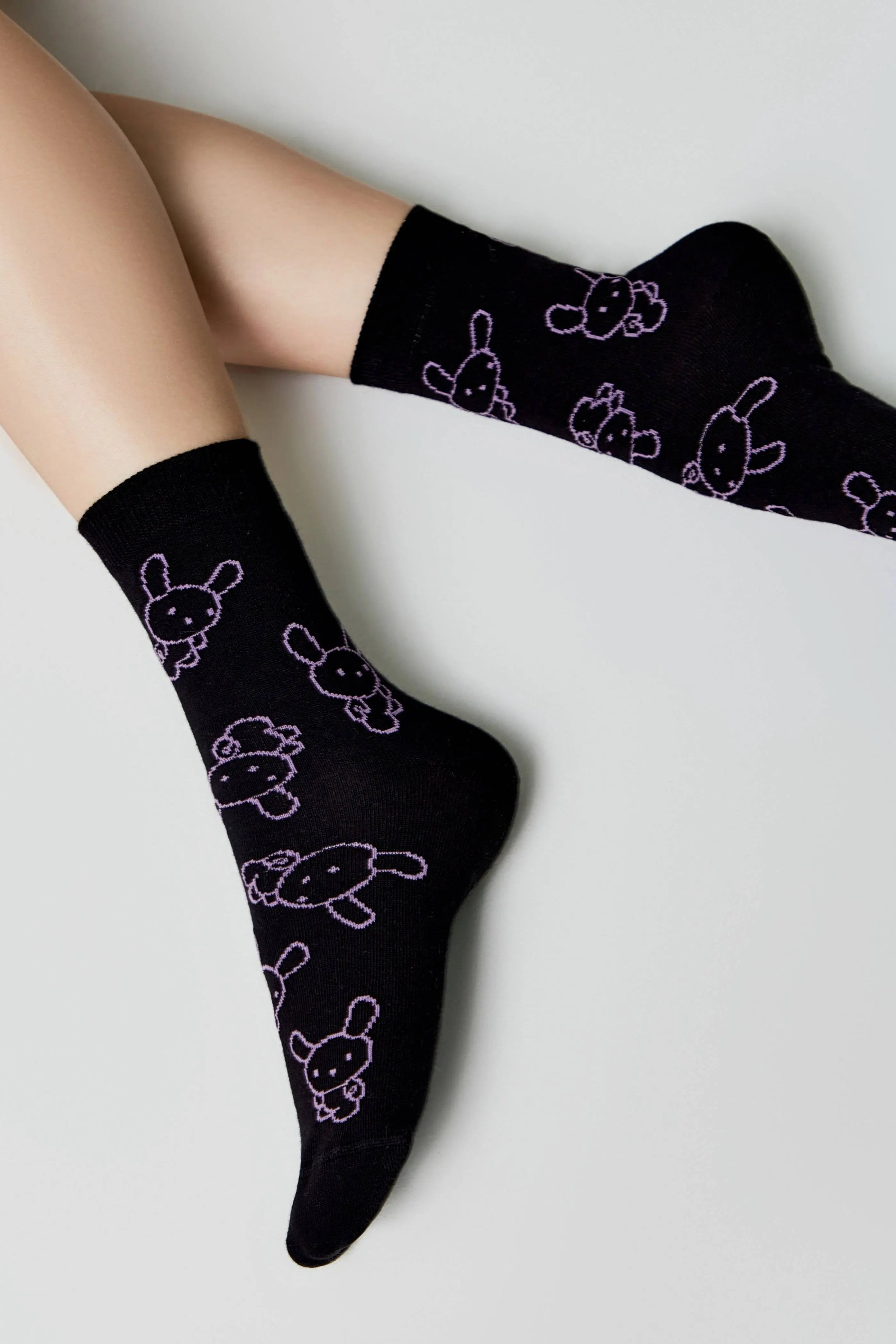 Black socks with white bunny designs worn by a person on a light gray background