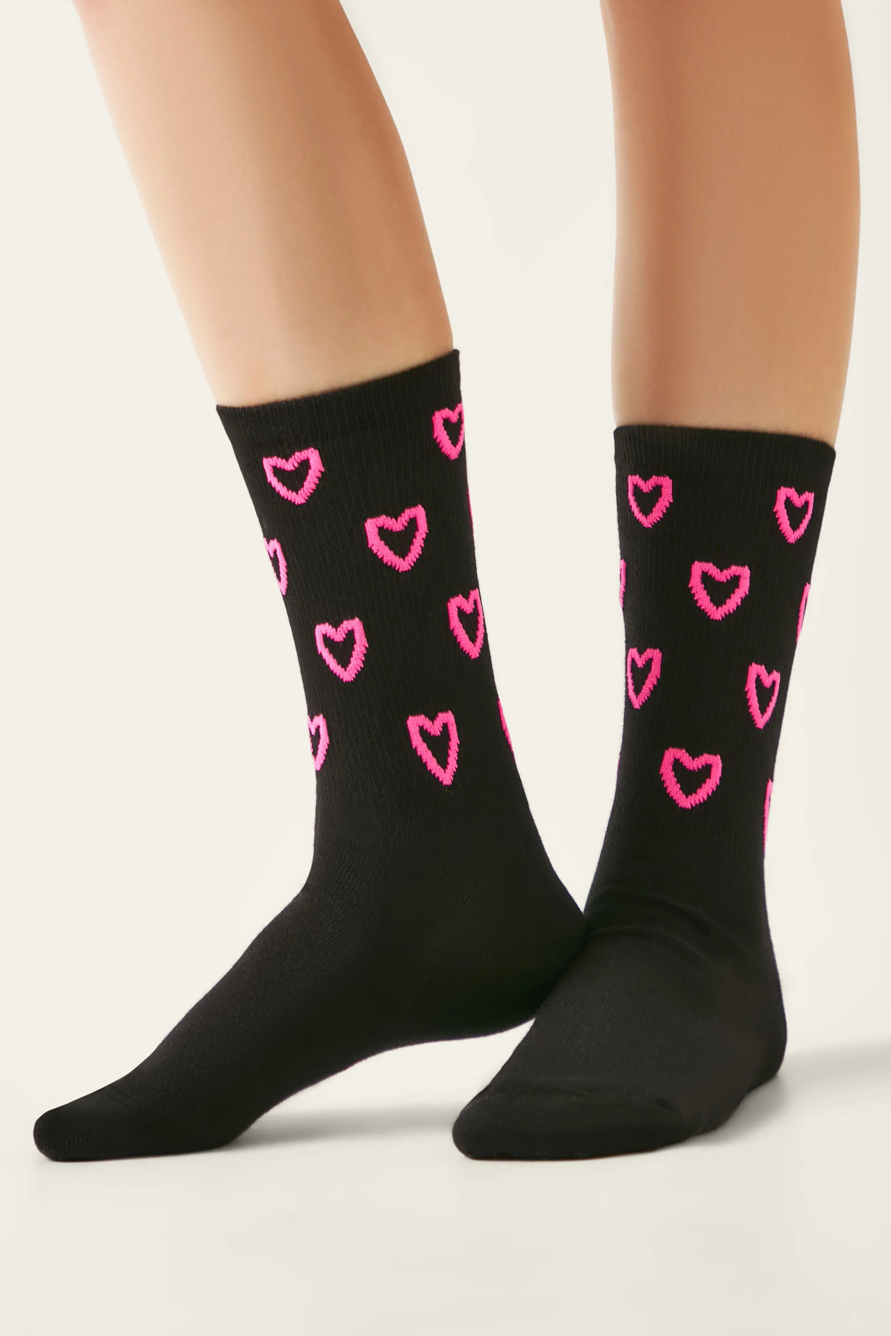 Black socks with pink heart patterns worn by a person on a light background #color_black