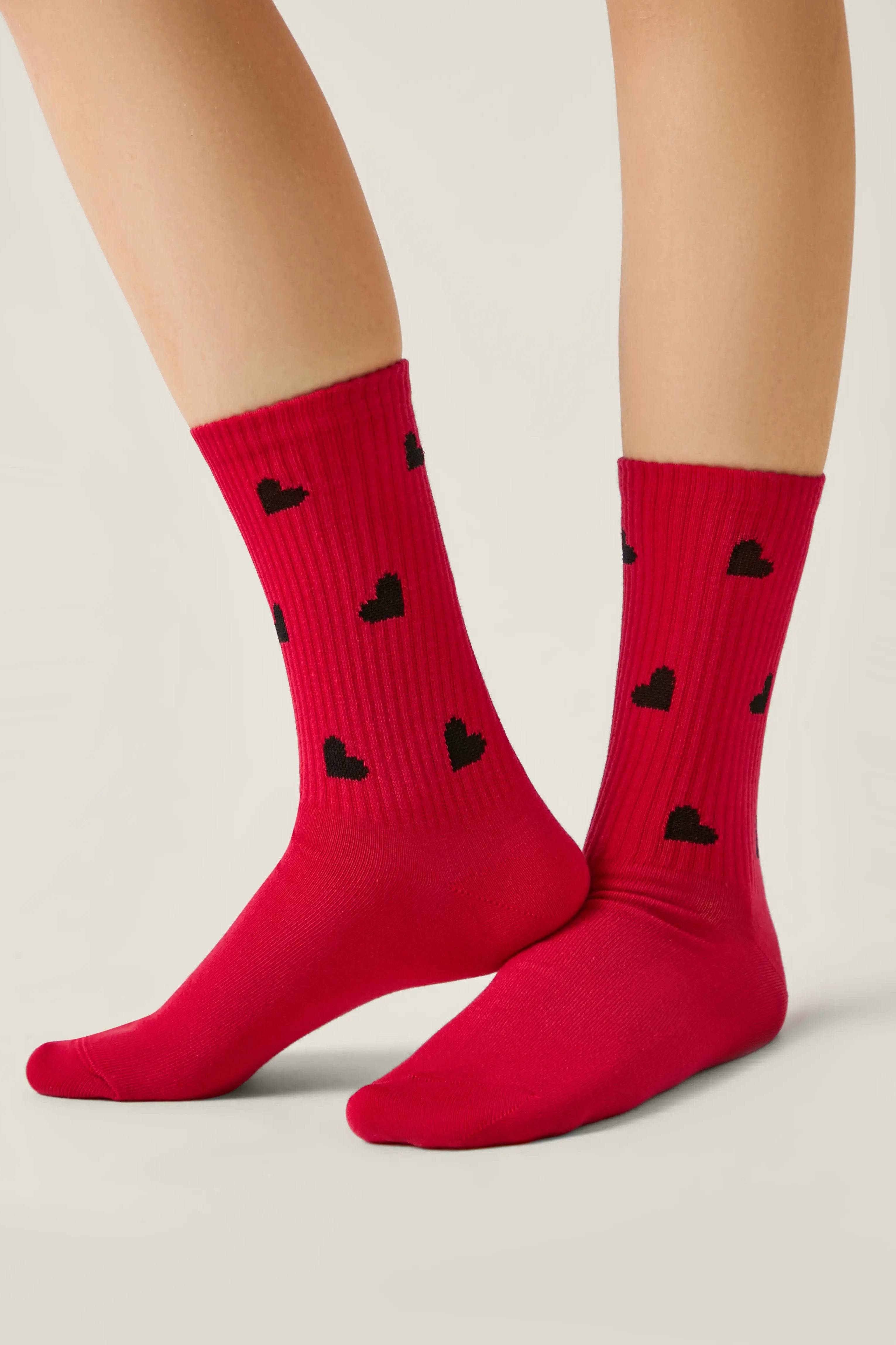 Red socks with black heart patterns worn by a person on a light gray background #color_red