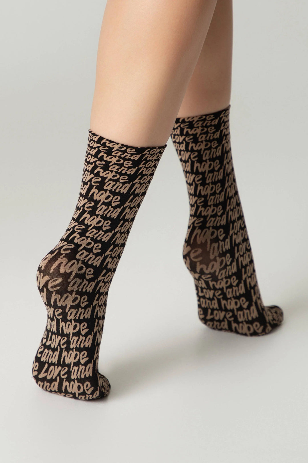 Black socks with text pattern worn by a person on a light gray background #color_nero-natural
