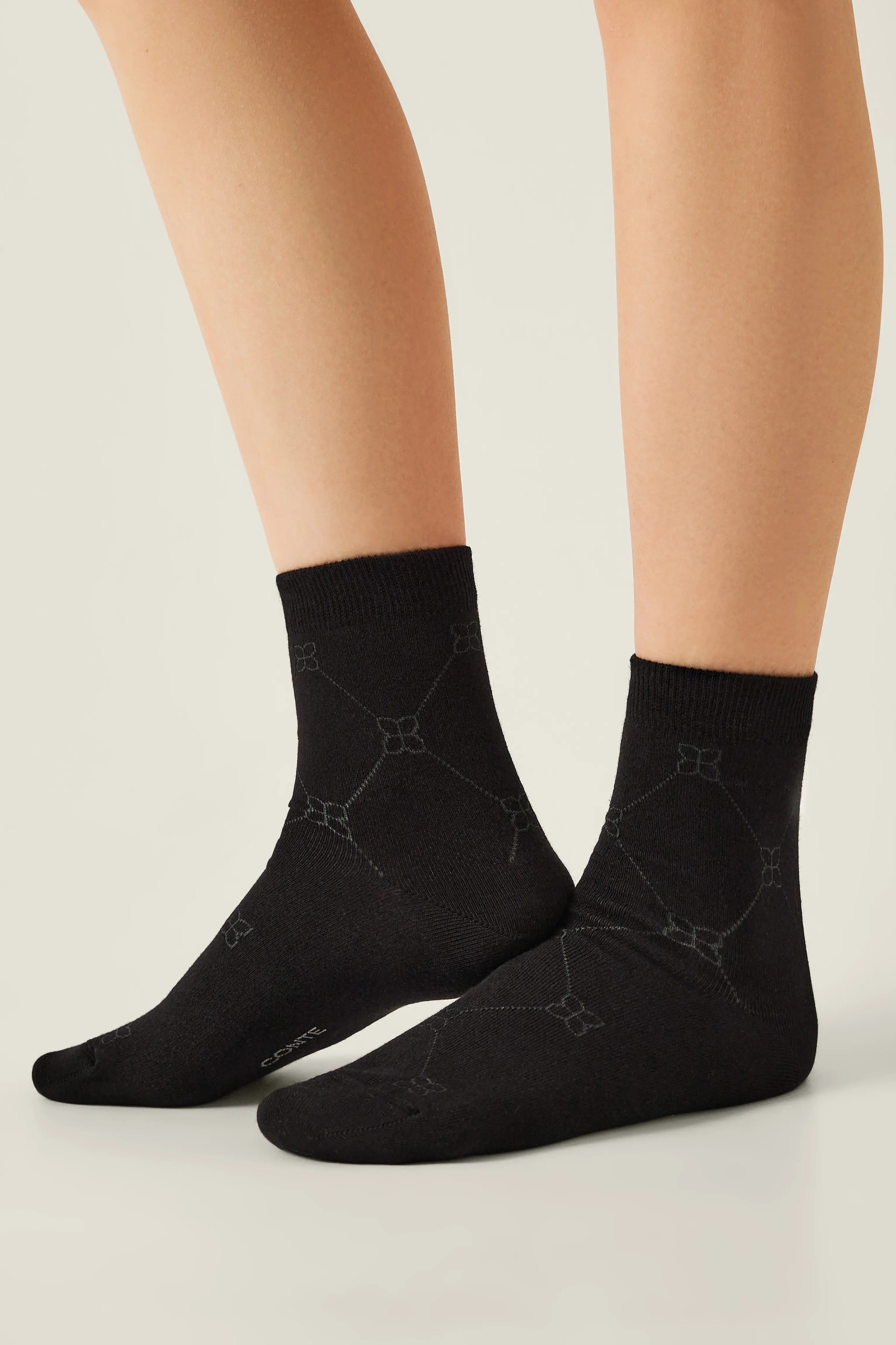 Black socks with a subtle pattern worn by a person on a light background #color_black
