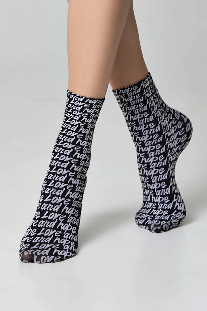 Black socks with white text worn by a person on a light gray background #color_nero-bianco