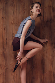 Woman in a sleeveless top and shorts posing against a wooden wall
