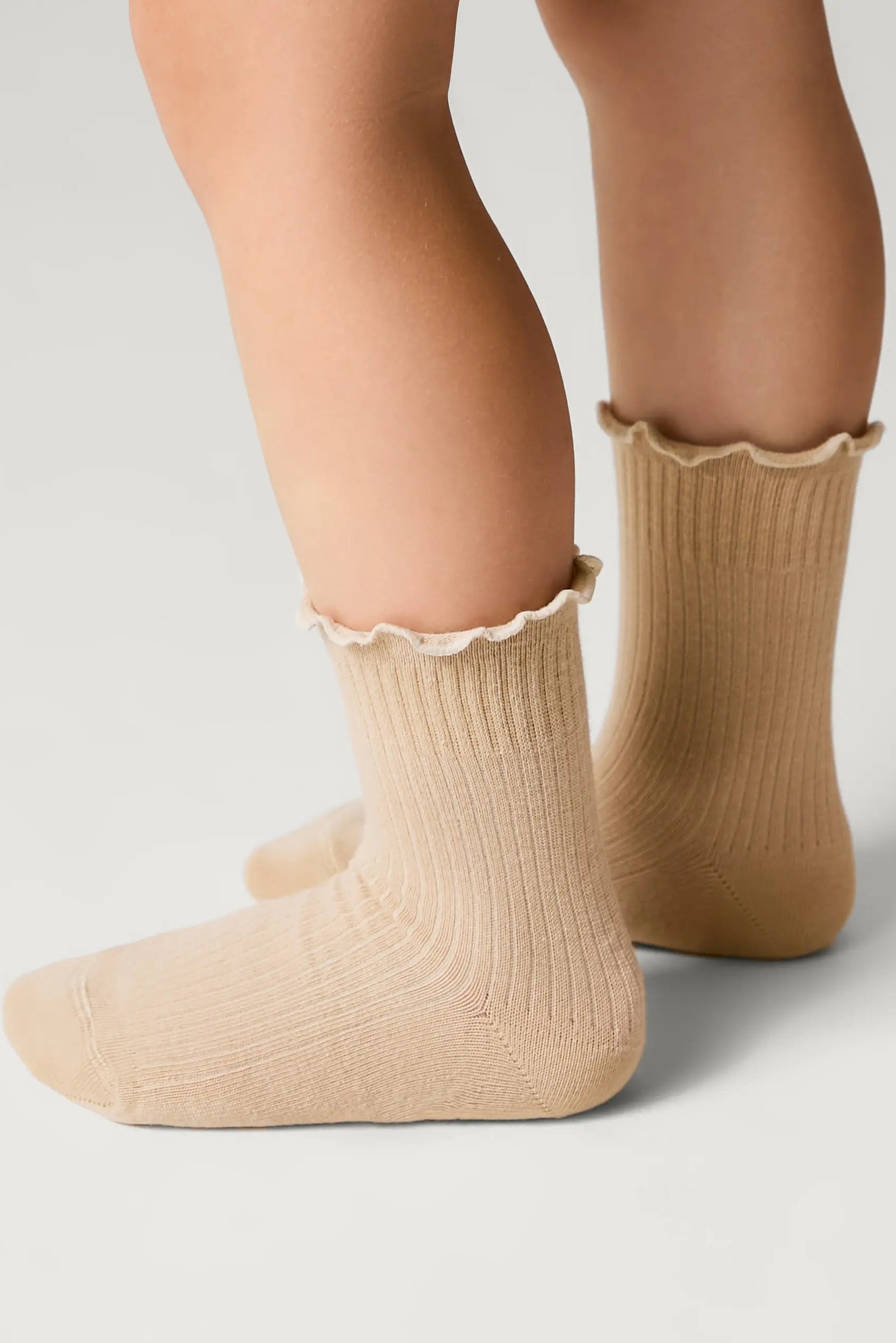 Beige socks with ruffled top worn by a person on a light gray background #color_beige