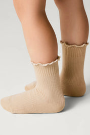 Beige socks with ruffled top worn by a person on a light gray background #color_beige