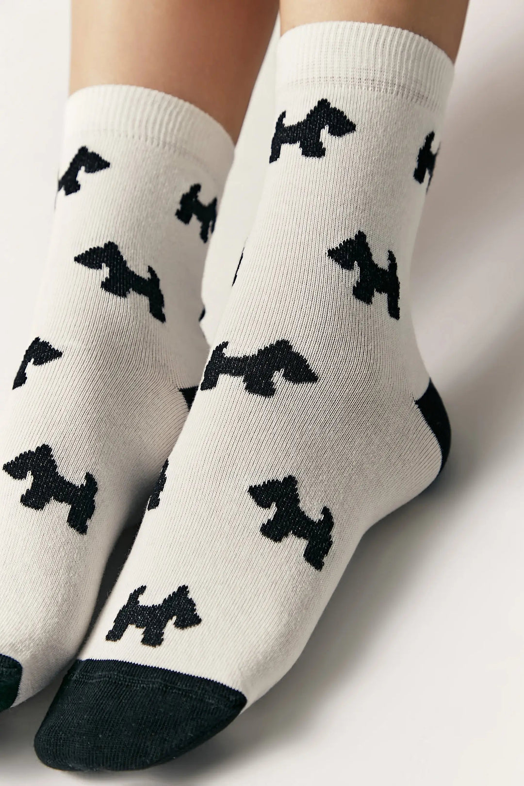 White socks with black dog pattern worn by a person on a light background #color_milk