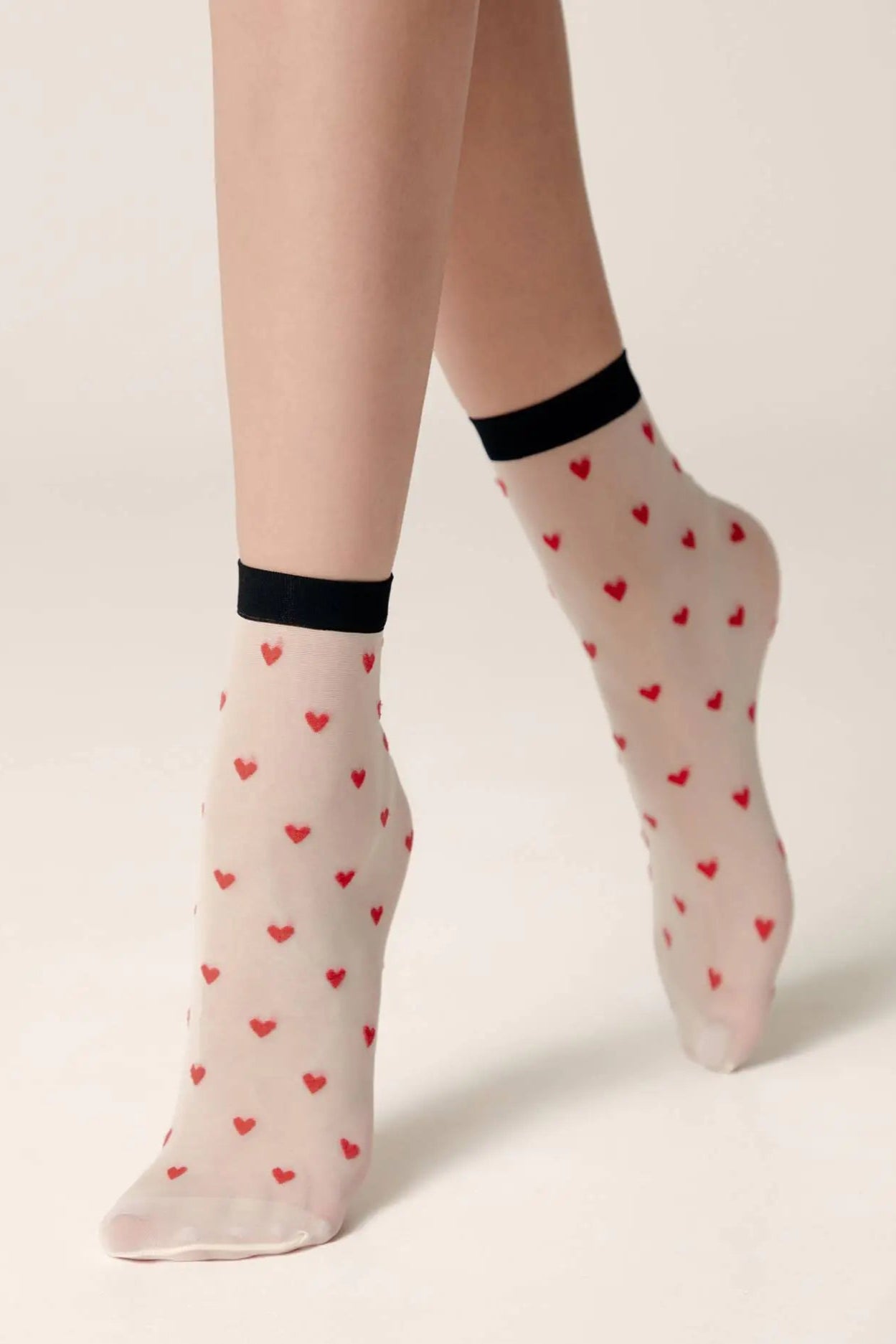 Sheer socks with red heart pattern worn by a person on a light background #color_panna