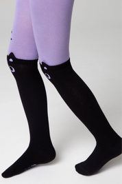 Black knee-high socks with white polka dots worn with purple tights on a light gray background
