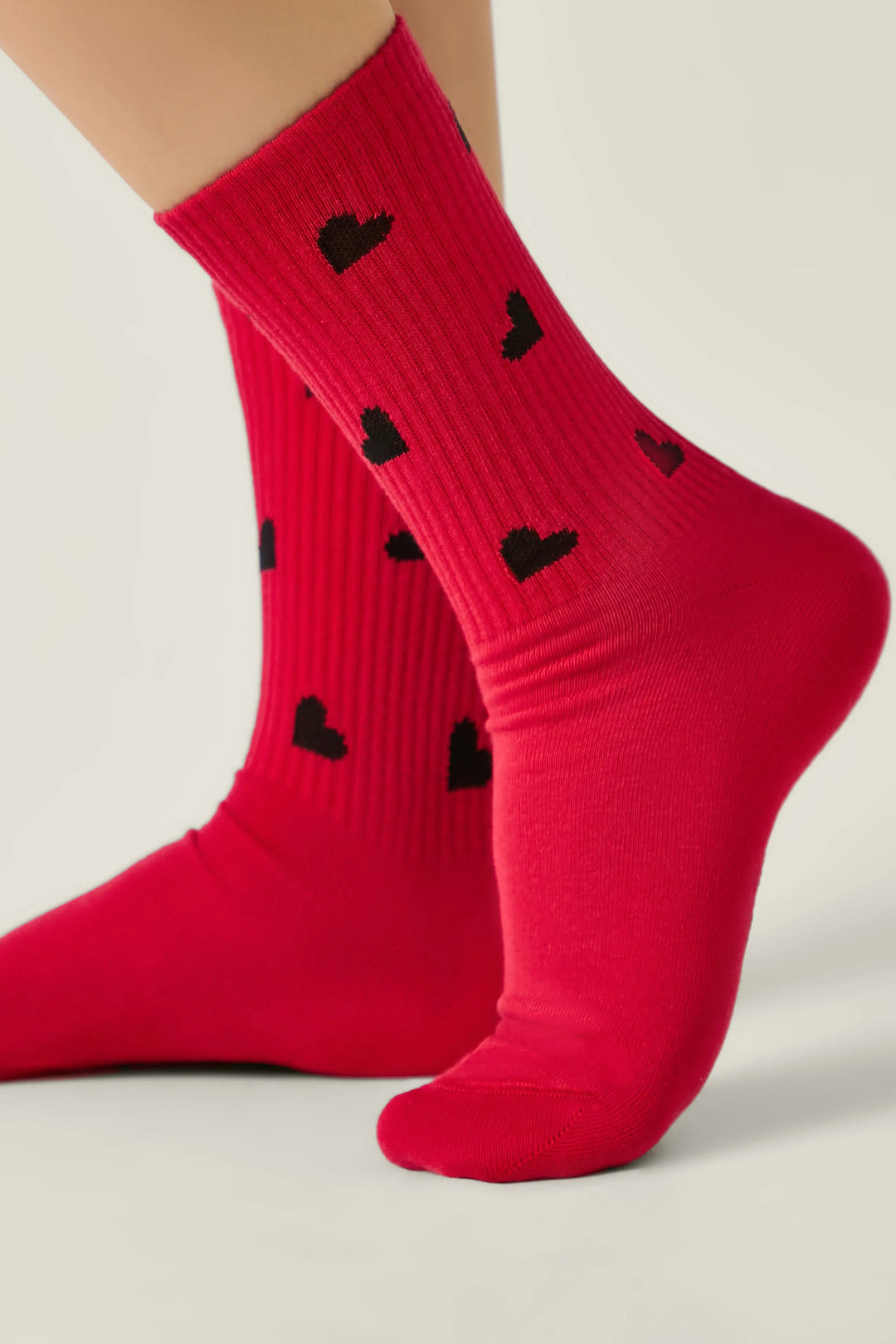 Red socks with black heart patterns worn by a person on a light background #color_red
