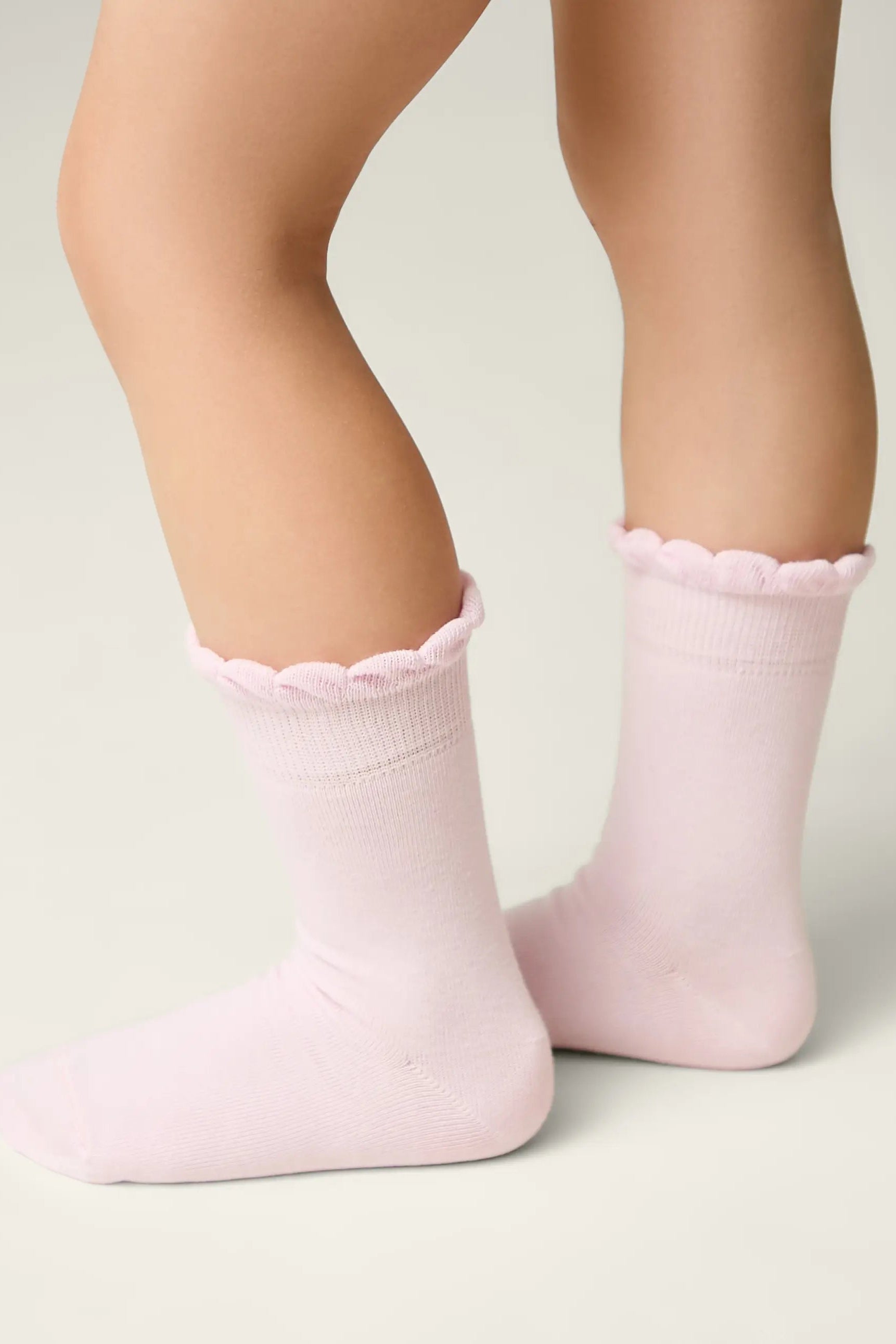 Pink socks with scalloped edges worn by a child on a light background #color_light-pink