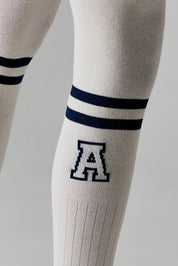 White knee-high socks with blue stripes and a logo on a neutral background