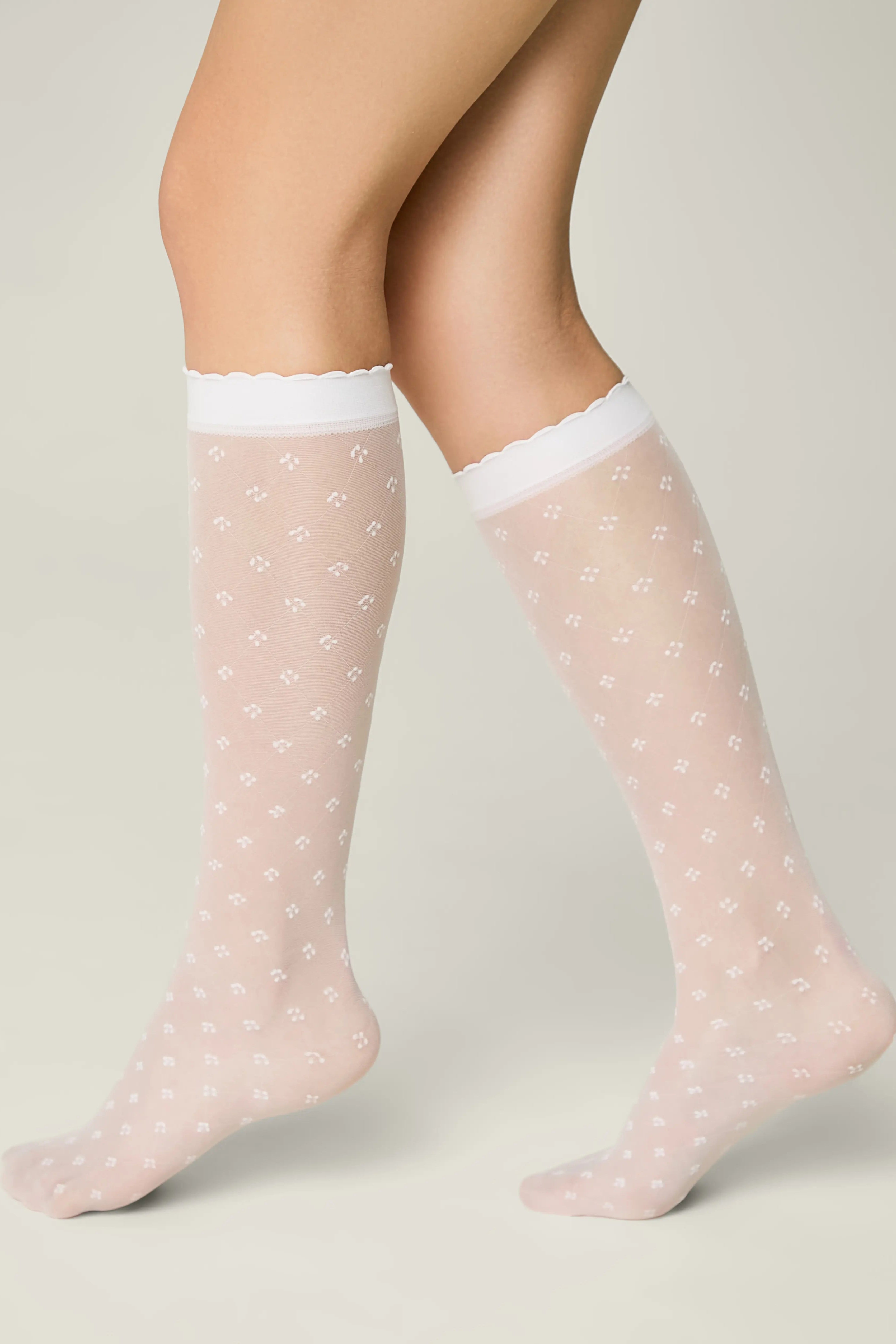 Pink sheer socks with white polka dots worn by a person on a neutral background #color_bianco