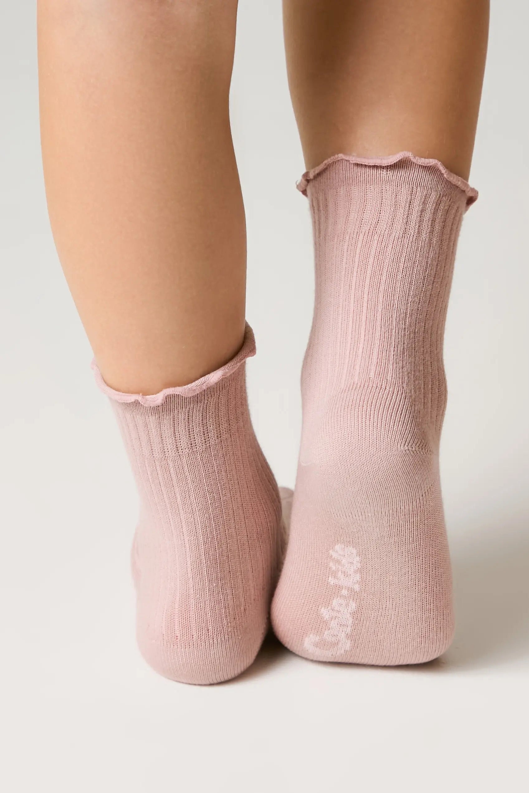 Pink socks with ruffled top worn by a person on a light background #color_ash-pink