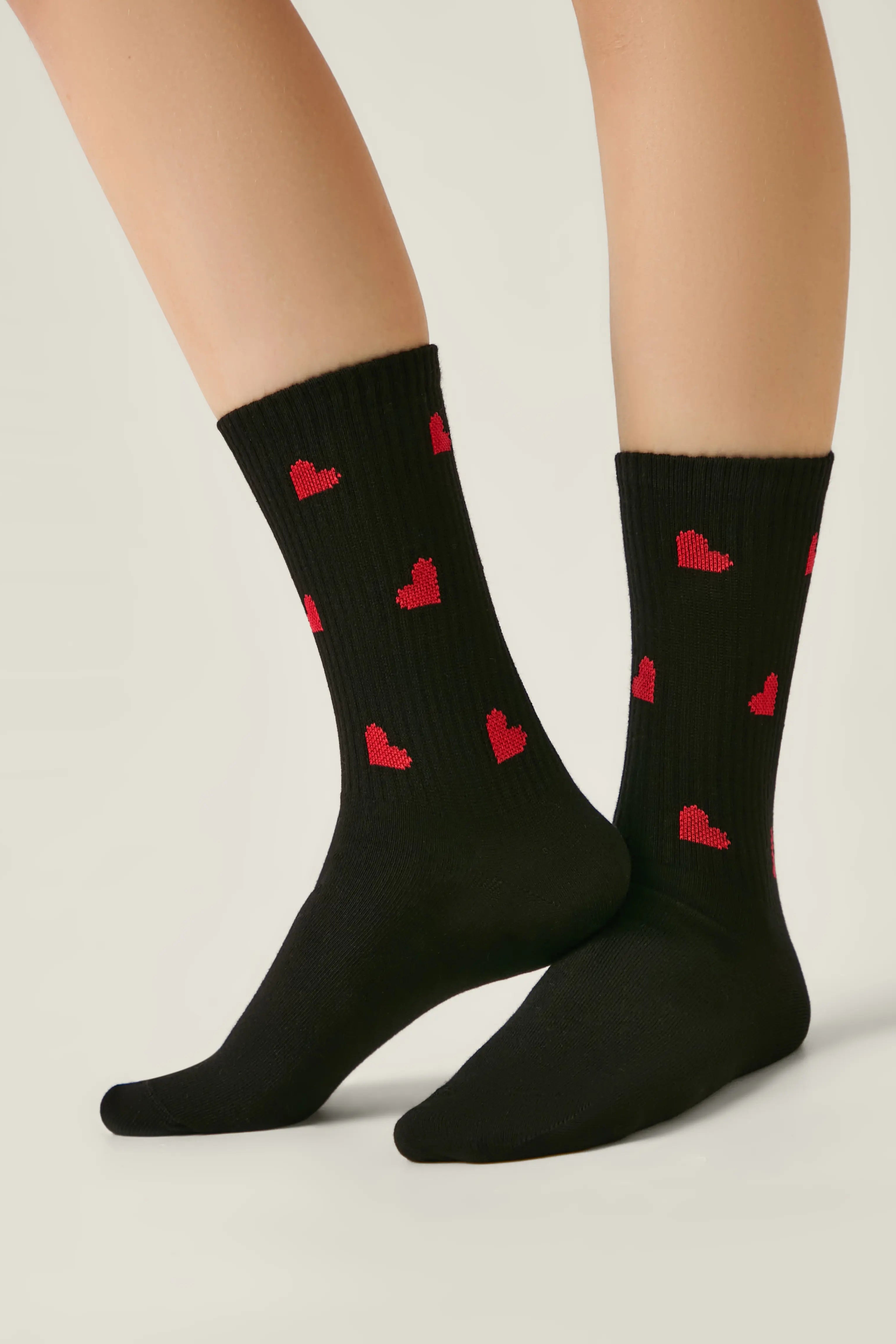 Black socks with red heart patterns worn by a person on a light gray background #color_black