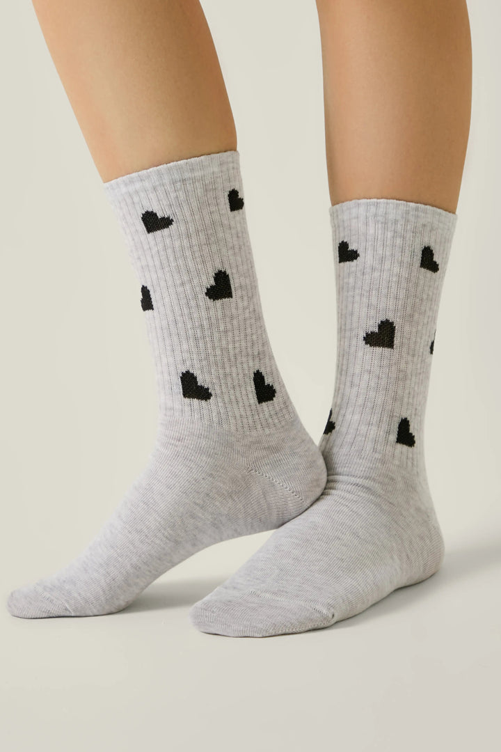 Gray socks with black heart patterns worn by a person on a neutral background #color_light-gray