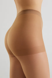 Close-up side view of a model wearing sheer, skin-toned compression hosiery or shapewear on the hip and upper thigh, against a light gray studio background.
