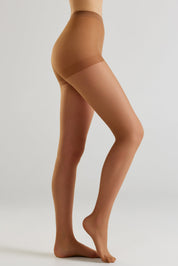 A side view of a model's legs wearing sheer skin-tone hosiery against a light gray studio background.