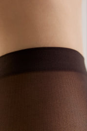 Close-up of sheer black tights worn on a leg, showing the elastic waistband and fine knit texture against skin.