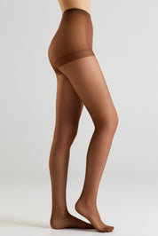 Side view of a model wearing sheer brown hosiery, showing the leg and foot against a light gray studio background.