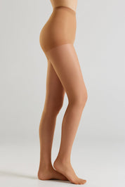 Side view of a model's legs wearing sheer, skin-toned hosiery against a light gray studio background.