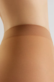Close-up of a model's hip and upper thigh wearing sheer nude hosiery with a wide, comfortable waistband against a light gray background.