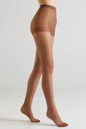 A model's legs wearing sheer, skin-toned hosiery with a darker brown waistband, shown from a side profile against a light gray studio background.