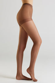 A model's legs wearing sheer brown hosiery, shown from the waist down in a side profile against a light gray studio background.