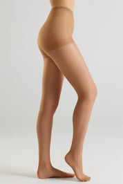 Side view of a model's legs wearing sheer, skin-toned hosiery against a light gray studio background.