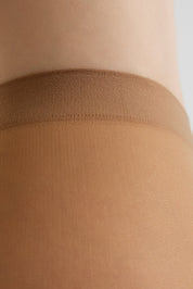 Close-up of a person's leg wearing a sheer nude beige hosiery stocking with a wide ribbed waistband.