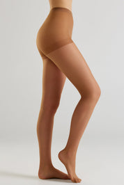 A side view of a model's legs wearing sheer skin-tone hosiery against a light gray studio background.