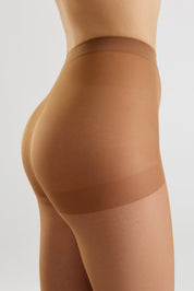 Close-up side view of a model wearing sheer tan compression hosiery with opaque support bands, shown against a light gray studio background.