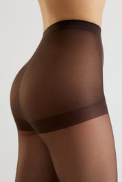 Close-up side view of a model wearing sheer dark brown hosiery with a wide opaque brown band at the upper thigh, against a light gray studio background.