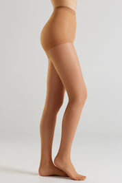 Side view of a model's legs wearing sheer, skin-toned hosiery against a light gray studio background.