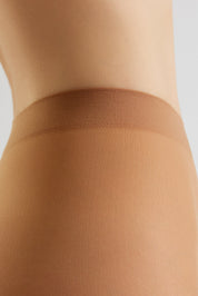 Close-up of a model's hip and upper thigh wearing sheer nude hosiery with a wide, comfortable waistband against a light gray background.