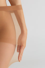 Close-up of a person wearing sheer nude hosiery with a wide elastic band, shown against a light gray studio background.