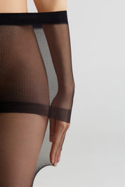 Close-up of a model wearing sheer black thigh-high stockings with opaque black bands, shown against a light gray studio background.