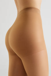 Close-up side view of a model wearing sheer nude tights against a light gray studio background.
