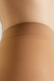 Close-up of a person's lower torso wearing sheer beige hosiery with a wide ribbed waistband.