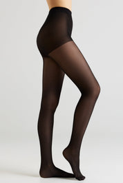 A model's legs wearing sheer black tights, shown from the waist down in a side profile against a light gray studio background.