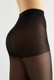 Close-up side view of a model wearing sheer black thigh-high stockings against a light gray studio background.