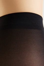 Close-up of a person's lower torso wearing sheer black hosiery with a wide black waistband.