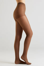 A model's lower body shown in side profile wearing sheer brown hosiery against a clean light gray studio background.