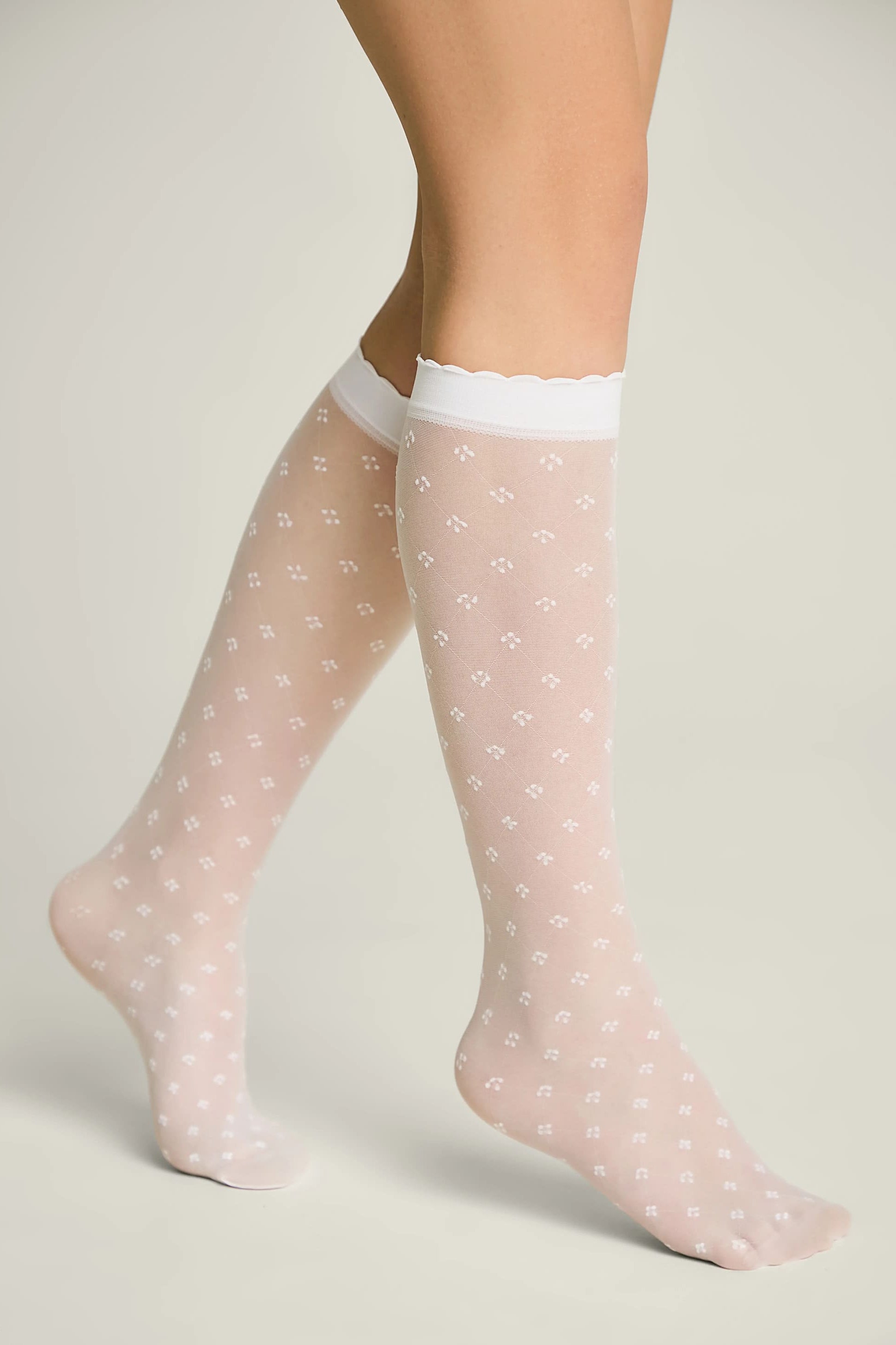 Sheer pink socks with white polka dots worn by a person on a light gray background #color_bianco