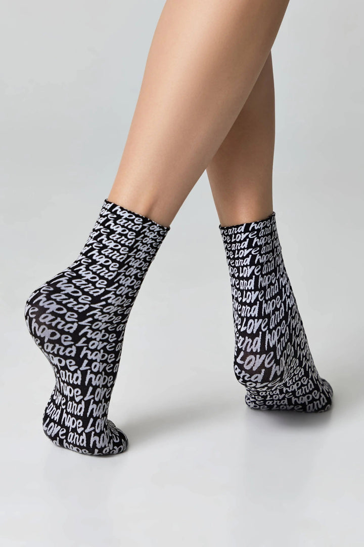 Black socks with white text worn by a person on a light gray background #color_nero-bianco