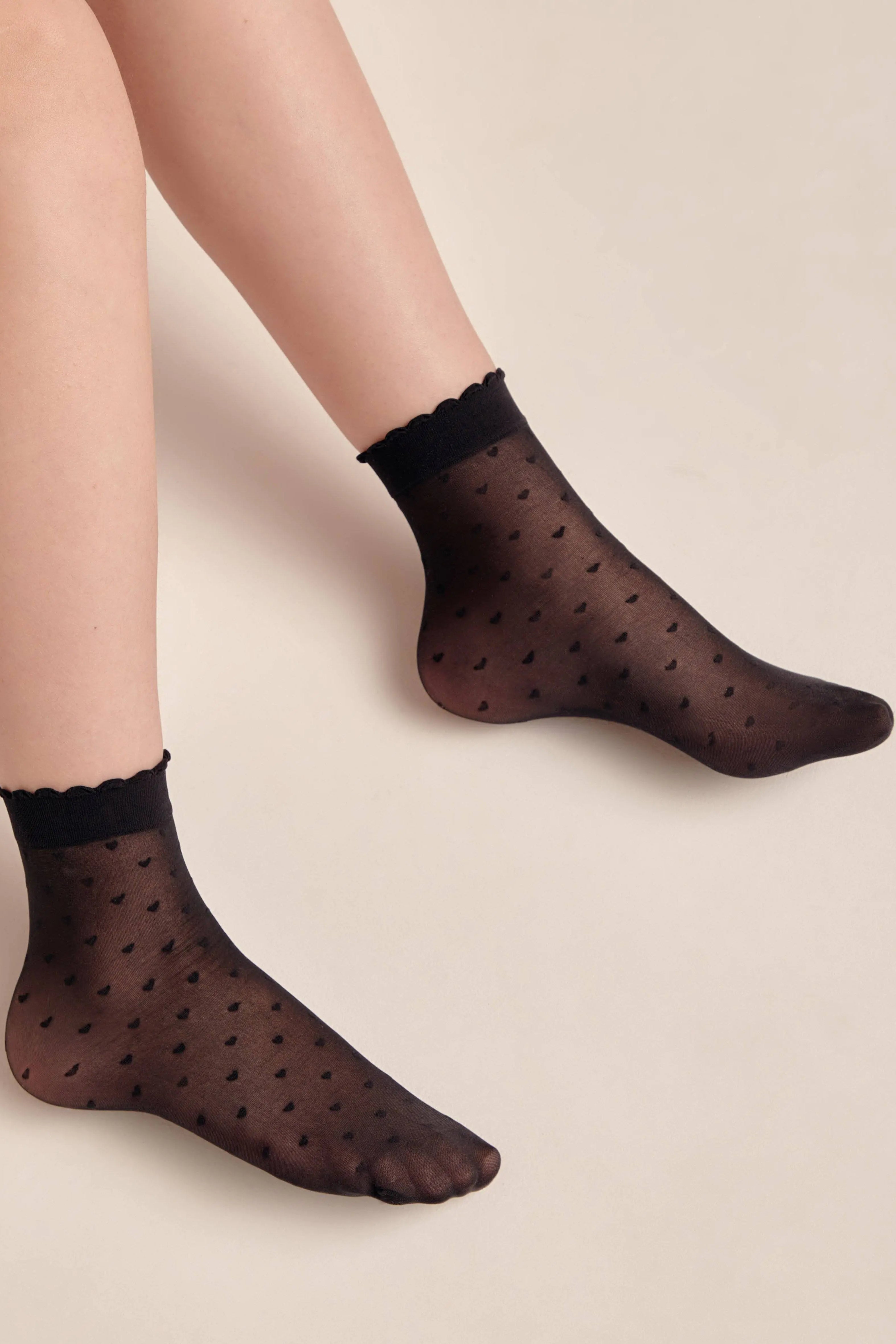 Black polka dot socks worn by a person on a beige background #color_nero-black