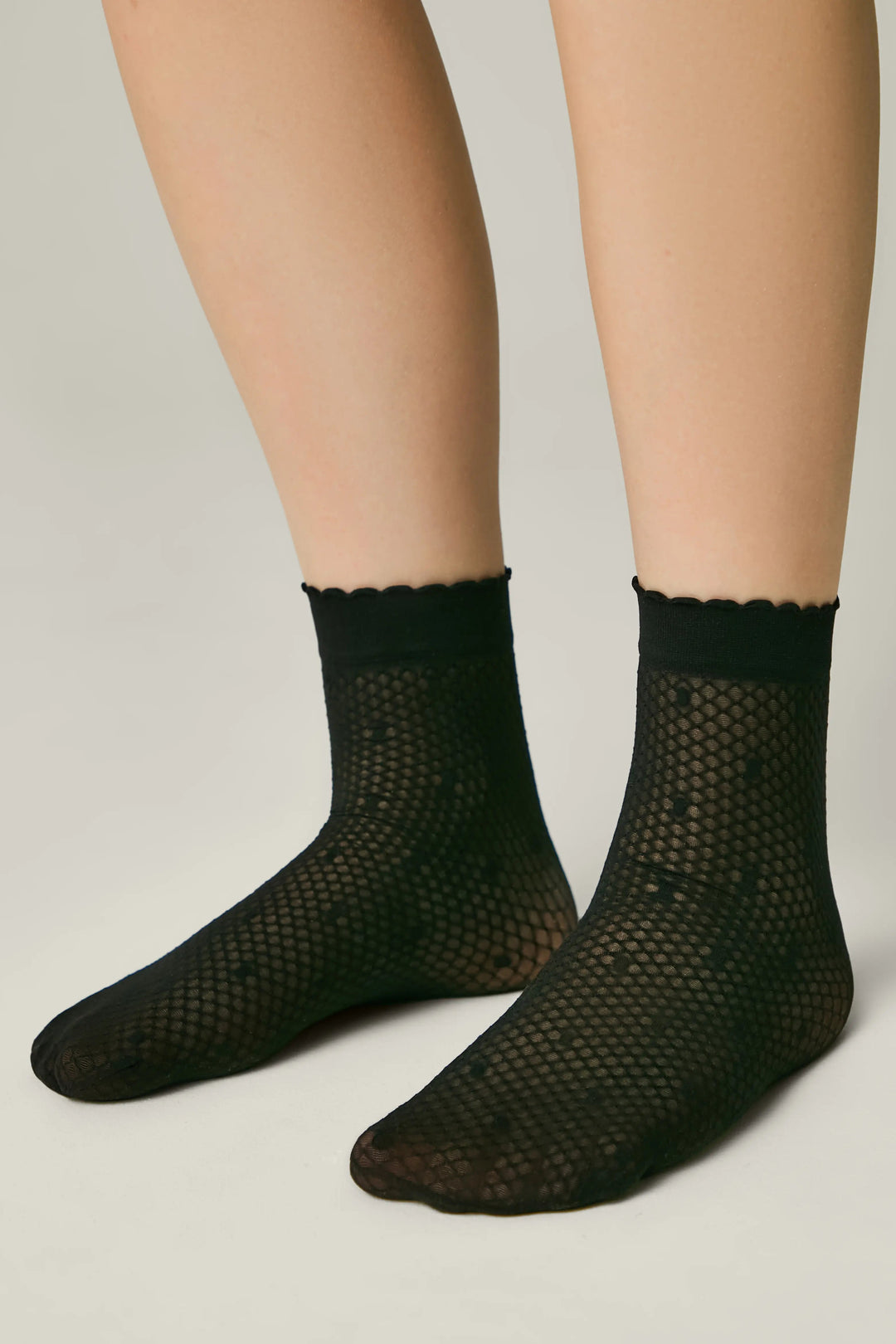 Black fishnet socks worn by a person on a plain background #color_nero-black