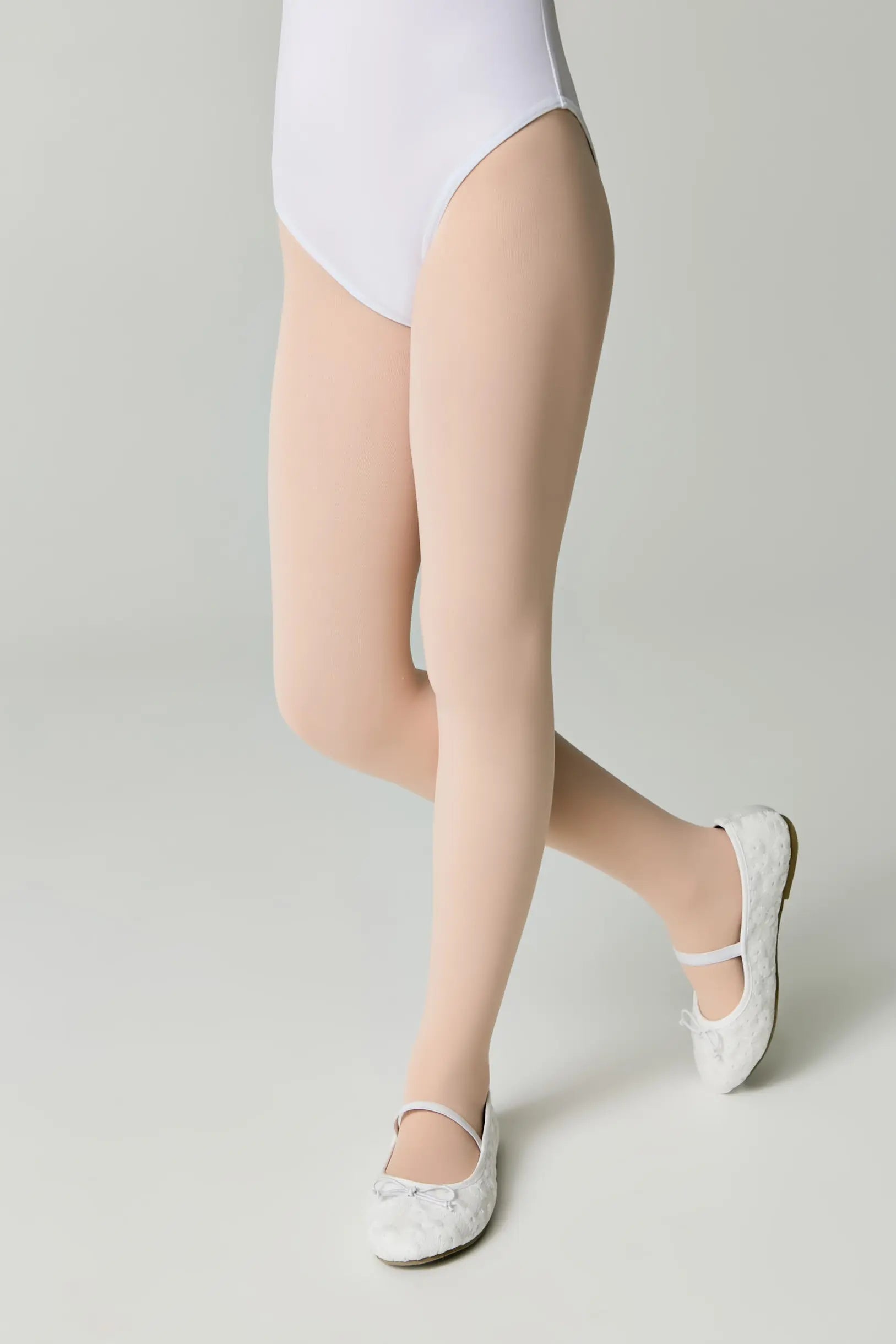 Person wearing beige sheer stockings with white shoes on a light gray background #color_pink-ballet