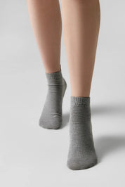 A pair of heather gray ankle socks worn on a model's feet, shown against a clean light gray studio background.