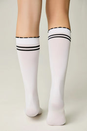 White knee-high socks with black stripes worn by a person on a plain background