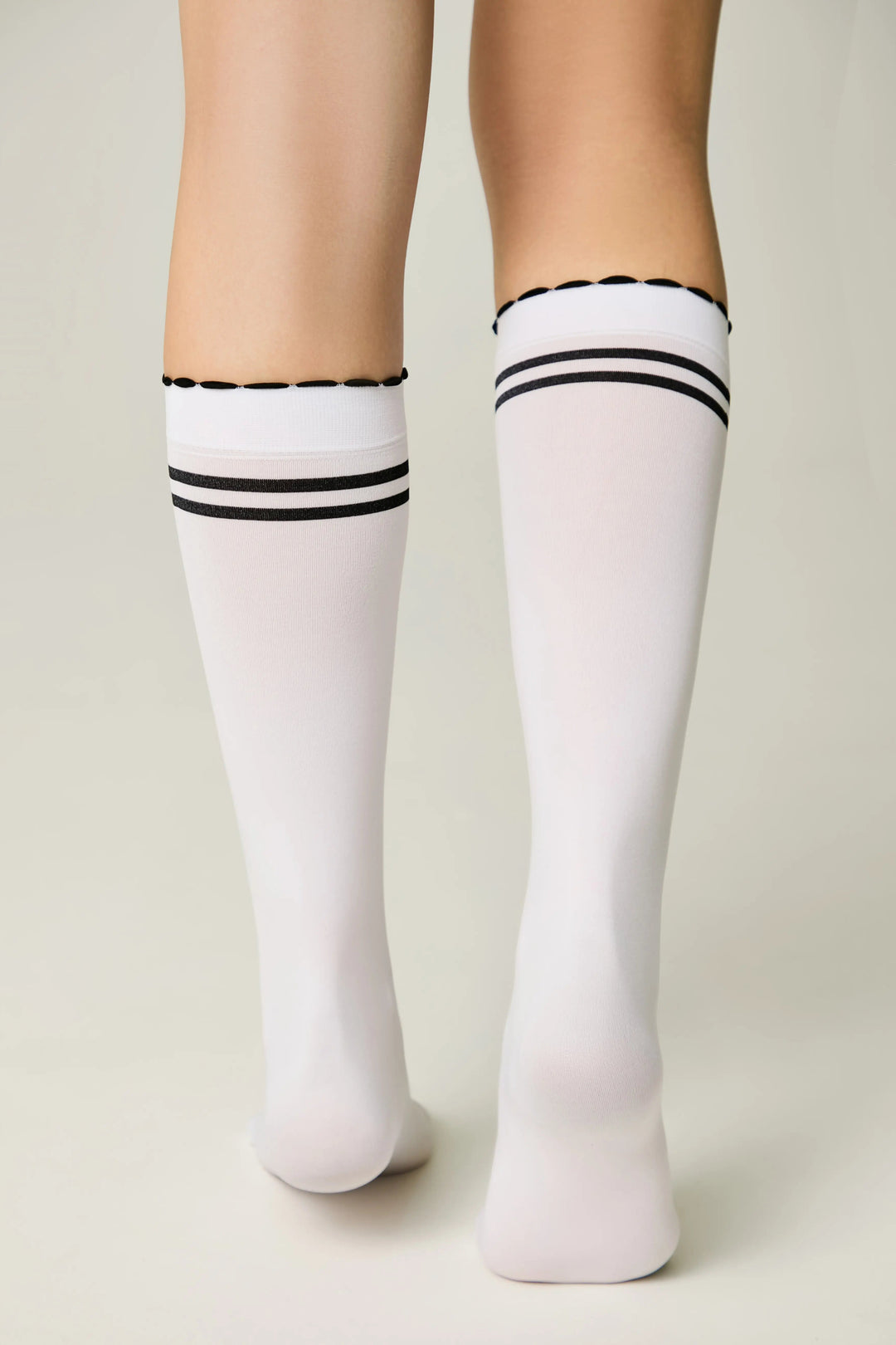 White knee-high socks with black stripes worn by a person on a plain background